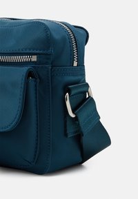 Borsa a tracolla in nylon teal con zip e dettagli metallici argentati, dotata di tasca laterale e tracolla regolabile, texture liscia.