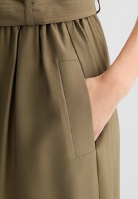 Gonna verde oliva con vita aderente e design plissettato, con una tasca laterale e tessuto a trama liscia.