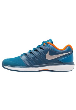 Men's athletic shoe in blue with gray accents, orange heel, textured fabric, and a white sole. Features a classic lace-up design.