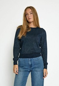 Granatowy metaliczny sweter z długimi rękawami i ściągaczami; dzianinowa tekstura; w zestawie z jasnoniebieskimi dżinsami o wysokim stanie.