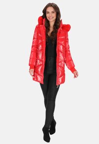 Piros, fényes, párnázott kabát szőrmével bélelt kapucnival, cipzáras elejű és kötött mandzsettás. Fekete leggings fölött viselve, karcsú, testhez simuló sziluettel.