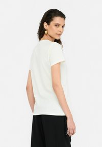 T-shirt beige clair à manches courtes avec un col rond, texture douce et coupe décontractée, associé à un pantalon noir. Design épuré et minimaliste.