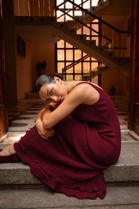 Bordeaux ribbel jurk met een mouwloze ontwerp en een gerimpelde zoom, gedragen terwijl ze op stenen trappen zit tegen een achtergrond van houten deuren.