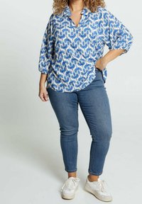 Camicetta a collare blu e bianca con motivo, maniche 3/4 e vestibilità rilassata, abbinata a jeans skinny blu e scarpe da ginnastica bianche.