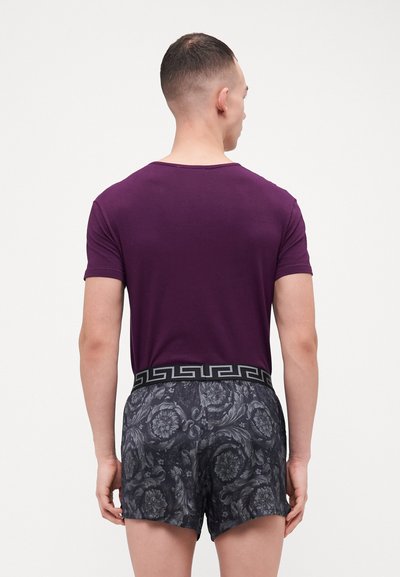 T-shirt en coton violet et shorts noirs à motifs avec une ceinture décorative. Les shorts présentent un motif floral dans des tons sombres.