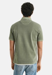 Kurzarm-Poloshirt aus olivgrünem Baumwollmaterial mit Kragen, gerippten Bündchen und schlichtem Rückendesign, kombiniert mit hellblauen Jeans.