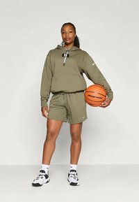 Sudadera color verde oliva y pantalones cortos de un tejido ligero, con un bolsillo frontal, y un balón de baloncesto etiquetado como "playground". Zapatillas negras y blancas.