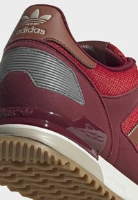 Detailní z�áběr na maroon tenisky Adidas s hnědým koženým detailem na patě, stříbrným reflexním štítkem a vzorem podrážky z gumové gumy.