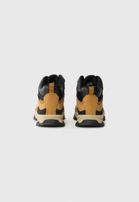 Pair of mustard and black hiking boots with beige soles, viewed from the back against a plain white background.
