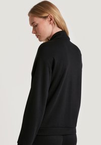 Maglione nero a collo alto con maniche lunghe e texture a coste. Presenta una vestibilità comoda e un tessuto liscio e morbido.