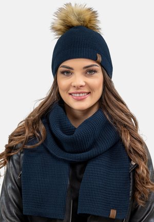 Beașcă tricotată bleumarin cu un pom-pom din blană sintetică și fular texturat asortat, ambele având un finisaj moale și detalii minime de branding.