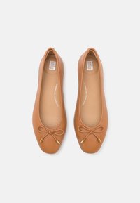 Mocasines de ballet de cuero marrón con punta redondeada, suela plana y un lazo con herrajes dorados, que cuentan con una textura suave y un diseño minimalista.