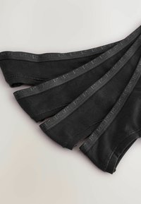 Calzini neri senza cuciture per caviglia disposti a ventaglio, con una superficie liscia e una fascia elastica morbida con un discreto dettaglio del logo.