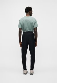 Camiseta de algodão verde claro combinada com calças pretas afuniladas, mostrando uma cintura elástica. As calças apresentam uma textura suave e um design justo.