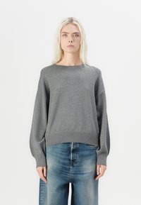 Hall griitest kootud sviiter ümmarguse kaelusega, laiad varrukad ja ribakujuline äär; koos helesiniste vabade teksadega. Lihtne, tekstuuriga disain.