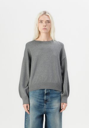 Grauer Strickpullover mit Rundhalsausschnitt, weiten Ärmeln und geripptem Saum; kombiniert mit hellblauen, locker geschnittenen Jeans. Einfaches, strukturiertes Design.