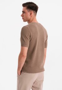 Suéter de punto texturizado de manga corta en marrón claro, con cuello redondo y diseño ajustado, combinado con pantalones beiges.