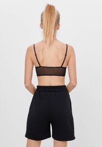 Černá síťová podprsenka s tenkými ramínky, spárovaná s černými šortkami vysokého pasu s elastickým pasem. Minimalistický design, bez vzorů.