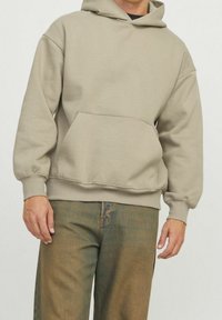 Sudadera beige hecha de una tela suave, presenta un bolsillo canguro, puños y dobladillo acanalados, con un corte relajado y capucha con cordones.