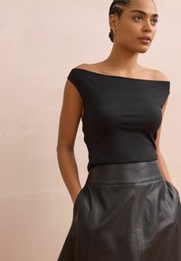 Top negro sin mangas hecho de una tela elástica, combinado con una falda de cuero negro de cintura alta con una textura suave y bolsillos.