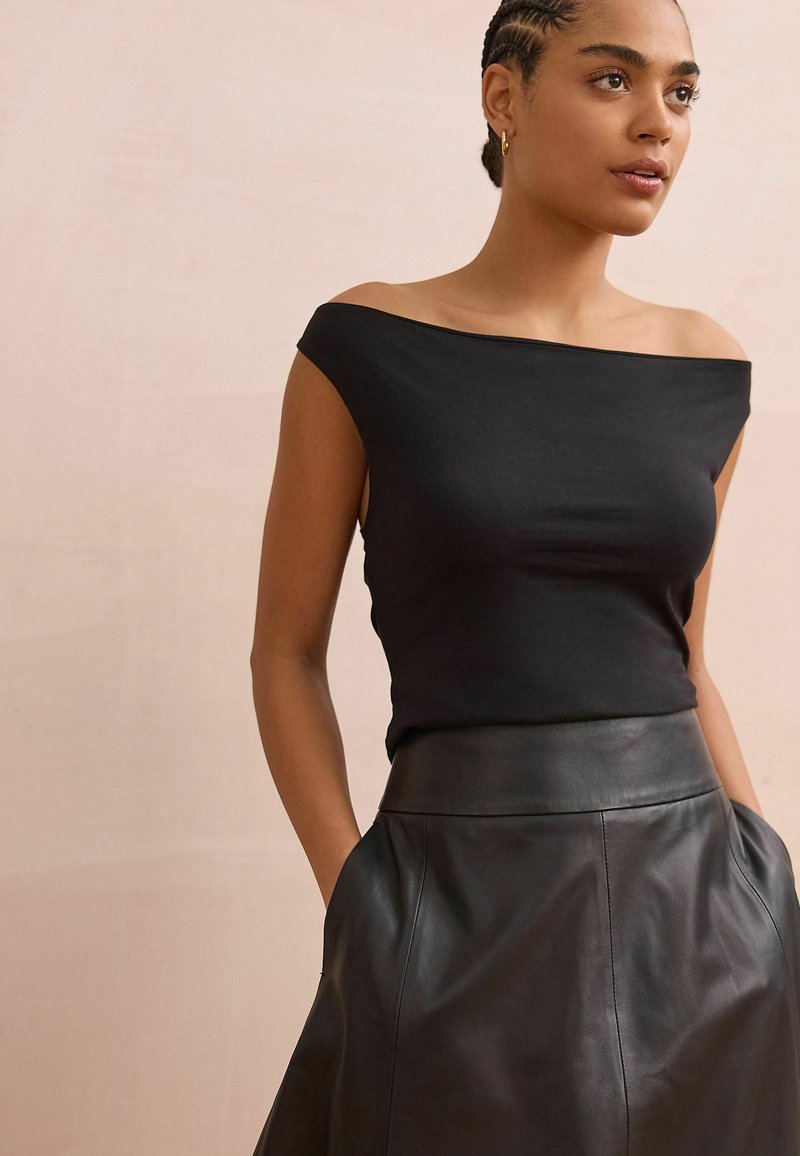 Top negro sin mangas hecho de una tela elástica, combinado con una falda de cuero negro de cintura alta con una textura suave y bolsillos.