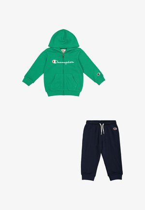 Felpa verde con zip e tasche frontali, con logo "Champion"; abbinata a pantaloni della tuta blu navy con cintura elastica e accento sul logo.