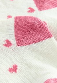 Strickstoff mit abwechselnden rosa und weißen Abschnitten, der kleine rosa Herzmuster für Textur und Designdetails aufweist.