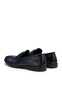 Scarpe slip-on in pelle nera con punta arrotondata, cuciture visibili e una superficie liscia. Presentano una fascia decorativa sulla parte superiore.