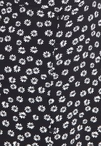 Černá tkanina s náhodně rozmístěnými bílými květinovými vzory sedmikrásek, s viditelným detailem knoflíku uprostřed. Hladká textura a přiléhavý střih.