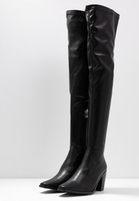 Bottes noires en similicuir montantes jusqu'à la cuisse avec un bout pointu et un talon bloc. Elles comprennent une fermeture éclair sur le côté et une texture lisse et brillante.