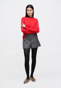 Suéter de punto rojo, pantalones cortos grises de talle alto, medias negras y zapatos slip-on con estampado de leopardo. Textura suave, diseño ajustado y estilo casual.