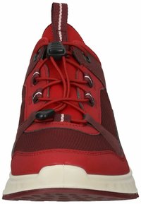 Scarpa sportiva rossa con tomaia in rete, suola in gomma, sistema di allacciatura e un occhiello per il tiraggio sul tallone. Presenta dettagli e texture contrastanti.