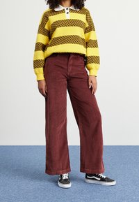 Yellow and brown striped sweater with a white collar, paired with maroon corduroy wide-leg pants and black sneakers.