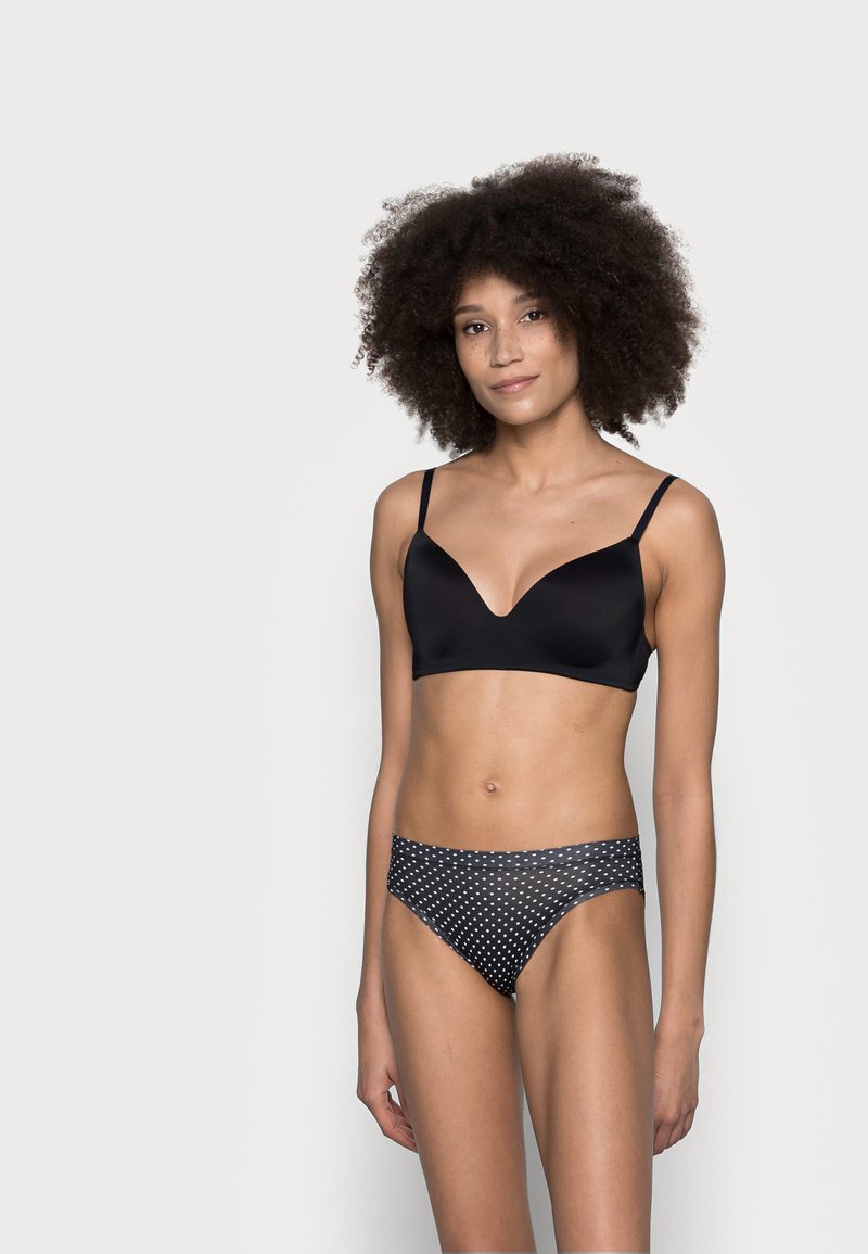 Reggiseno nero liscio con spalline sottili e scollatura a V profonda, abbinato a slip bikini neri con pois. Presenta un design senza cuciture e una forma aderente.