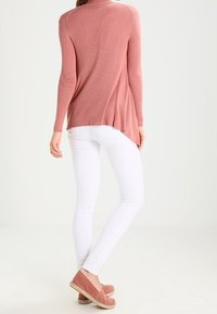 Suéter rosa con canalé y cuello alto, combinado con jeans ajustados blancos y alpargatas color rosa palo con suela de esparto. Vista trasera mostrada.