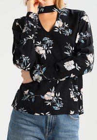 Schwarze Bluse mit Blumenmuster, V-Ausschnitt und Choker-Detail, mit hellrosa und blauen Blumenmustern auf einem weichen Stoff, langen Ärmeln und Knopfverschluss.