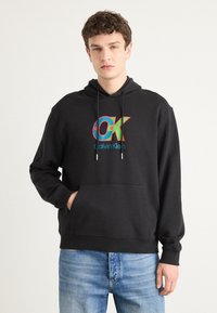 Fekete kapucnis pulóver színes "OK" logóval és kék "Calvin Klein" felirattal, elülső kenguruzsebbel és húzózsinóros kapucnival.