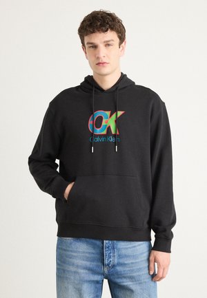Zwarte hoodie met een kleurrijk "OK" logo en "Calvin Klein" tekst in het blauw, met een voorkangoeroezak en een capuchon met koord.