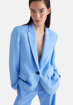 Blazer blu su misura in tessuto liscio con revers a contrasto, chiusura a singolo bottone e due tasche frontali. Presenta una vestibilità rilassata e un design minimal.