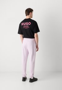 Sort t-shirt med pink "HUGO" tekst på ryggen, parret med lyserøde joggingbukser og sorte sneakers, der har elastiske mansjetter og sidelommer.