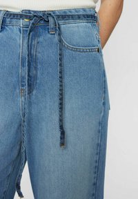 Hellblaue Denim-Hose mit hoher Taille, geflochtenem Bindegürtel und sichtbaren Nähten. Enthält Vordertaschen und ein entspanntes Design.