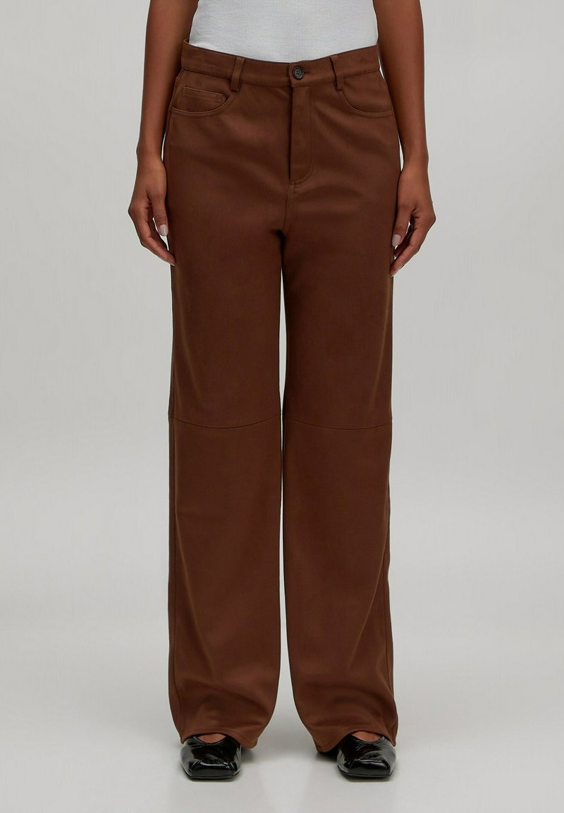 Braune weit geschnittene Hose mit glatter Textur, ausgestattet mit einem frontalen Knopfverschluss, zwei vorderen Taschen und einem minimalistischen Design.