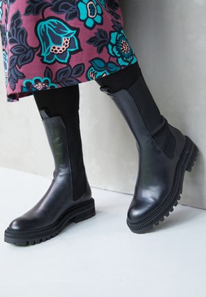 Schwarze Leder-Stiefeletten mit elastischen Seiteneinsätzen und strukturierten Gummisohlen. Sie verfügen über eine glatte Oberfläche und genähte Details entlang der Kanten.