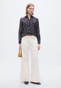 Blusa azul-marinho com padrão floral, abotoamento frontal, mangas compridas; combinada com calças largas creme e uma pequena mala amarela. Sapatos pretos.