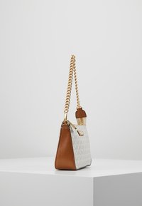 Světle hnědá a krémová kabelka s texturovaným vzorem loga, zlatým řetízkovým popruhem, hladkým povrchem a trojúhelníkovým tvarem. Má malý zlatý kovový detail.