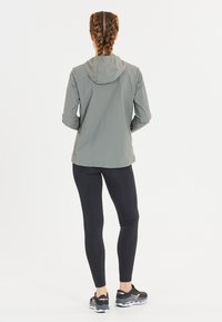 Ljust grå vindjacka med huva, kombinerad med svarta leggings och svarta träningsskor med rosa accenter. Slät textur, åtsittande design.