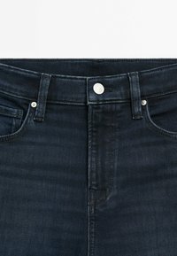 Dark denim jeans with a fitted design, featuring a front button and zipper closure, belt loops, and traditional five-pocket styling.