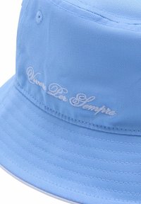 Jasnoniebieska czapka z szerokim rondem, uszyta z gładkiego materiału, z białym haftem w stylu kursywnym. Rondo jest szerokie, z teksturowanymi detalami w przeszyciach.