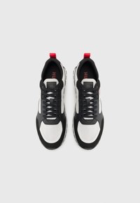 Svart-hvite sneakers med en teksturert overflate, med snøring, røde detaljer og et merketikett på tungen.