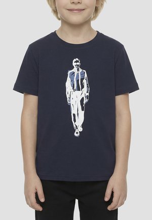 Bambino che indossa una maglietta blu navy con una grafica astratta bianca e blu di un uomo che cammina stampata sul davanti.